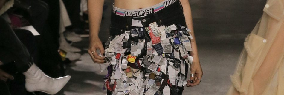 fashion show, girl walking with very exotic black pants with news paper pieces attached to it. Red Shirt with graphics on it.