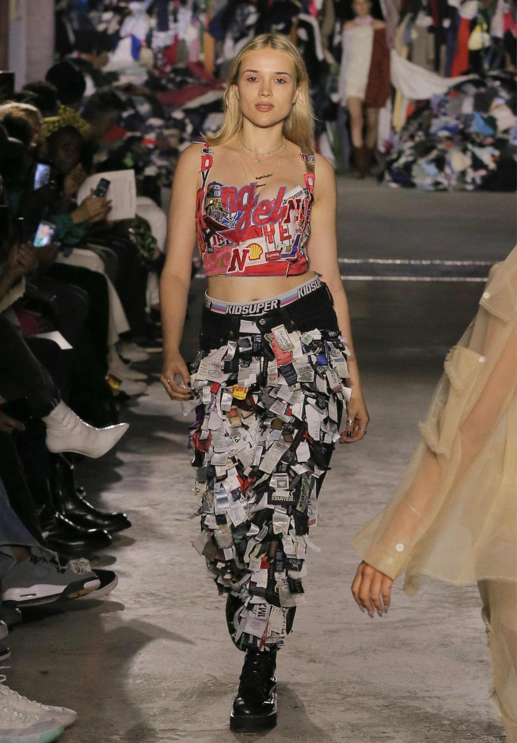 fashion show, girl walking with very exotic black pants with news paper pieces attached to it. Red Shirt with graphics on it.